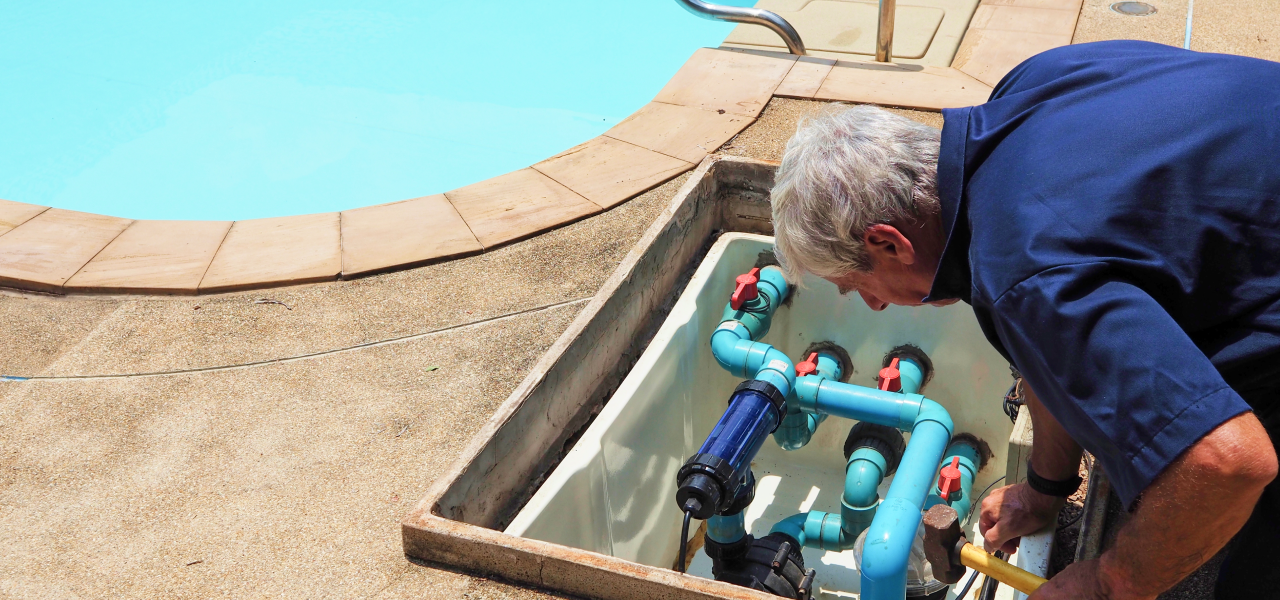 Pool technician inspecting underground pump and pipes, showing tasks that require professional service for seasonal care.