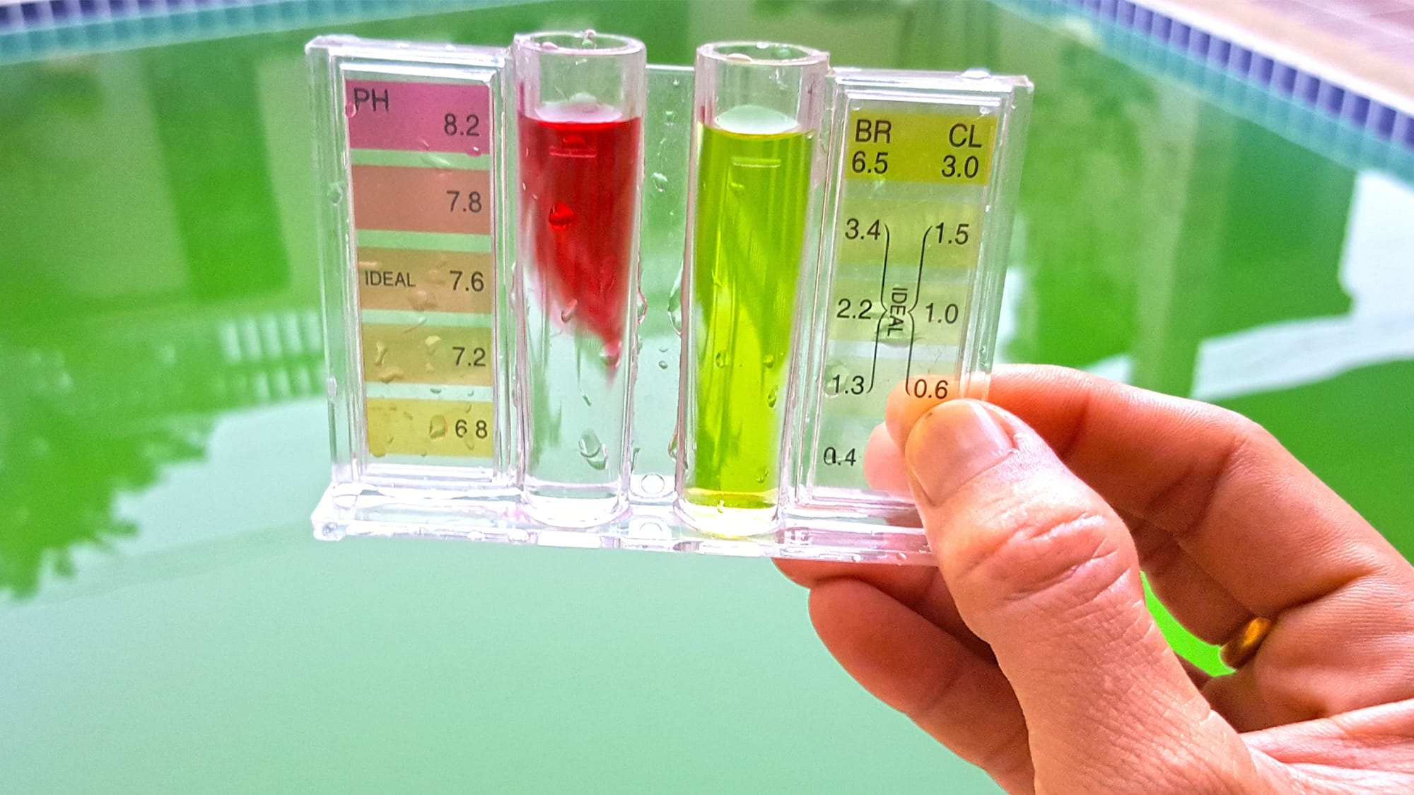 Hand holding a pool water test kit to check pH and chlorine levels above a swimming pool.