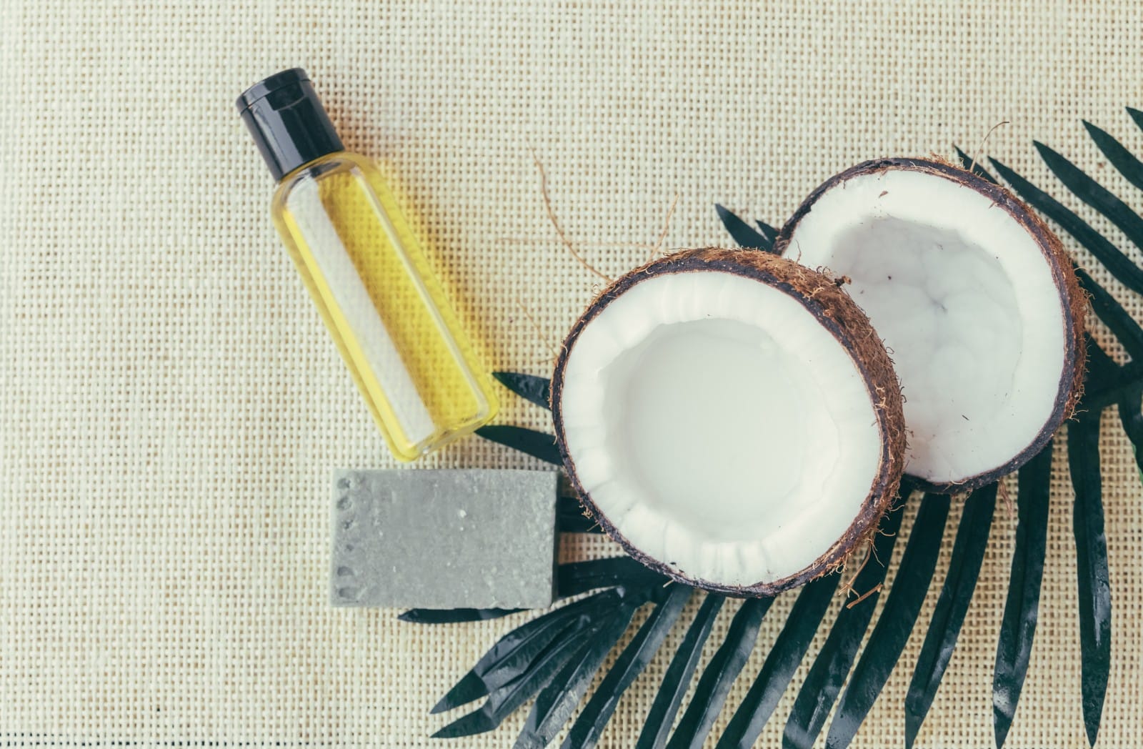 Flat lay of coconut oil, soap, and fresh coconuts, representing the natural oils and sealants used for pre-swim protection against chlorine damage.