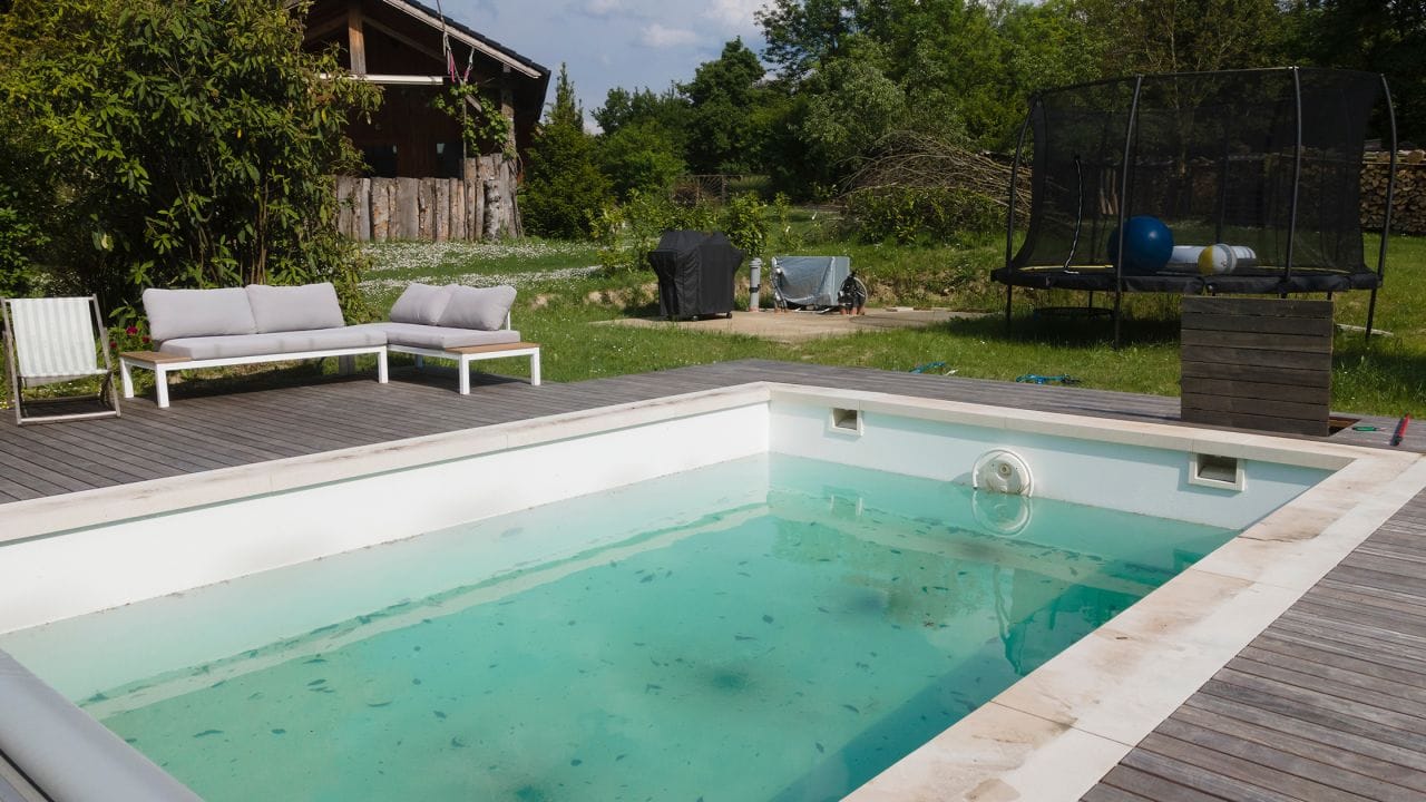 A dirty, hazy in-ground pool with visible debris and a green tint, indicating a phosphate-fueled algae problem.