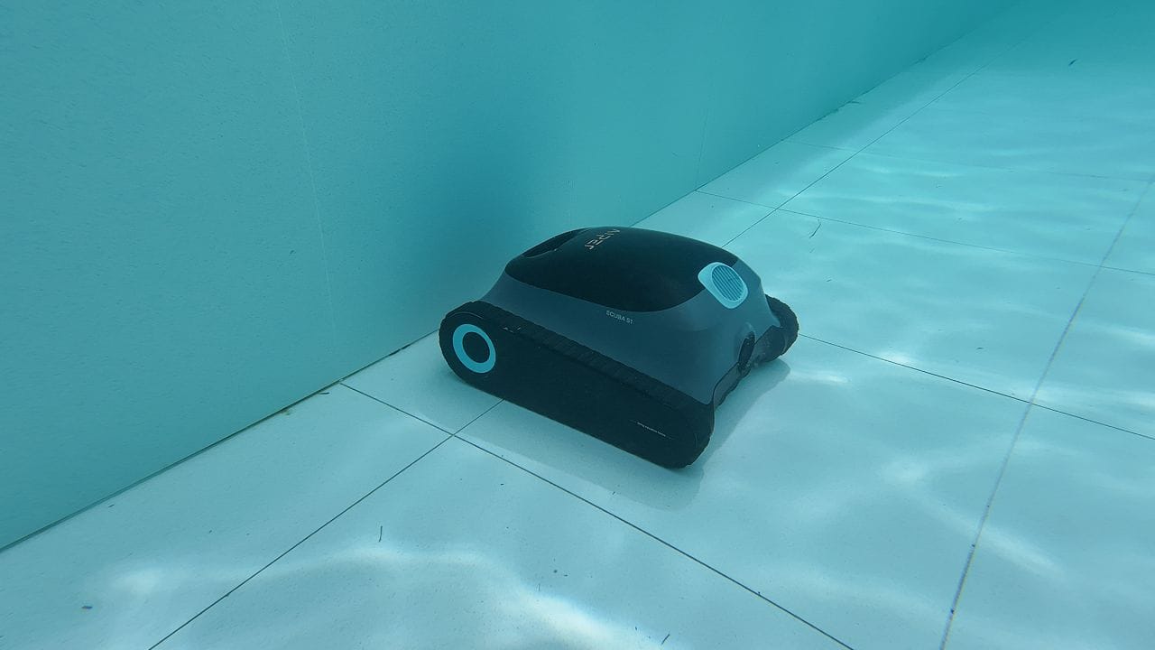 a modern robotic pool cleaner on the floor of a pool, actively vacuuming up small leaves and debris
