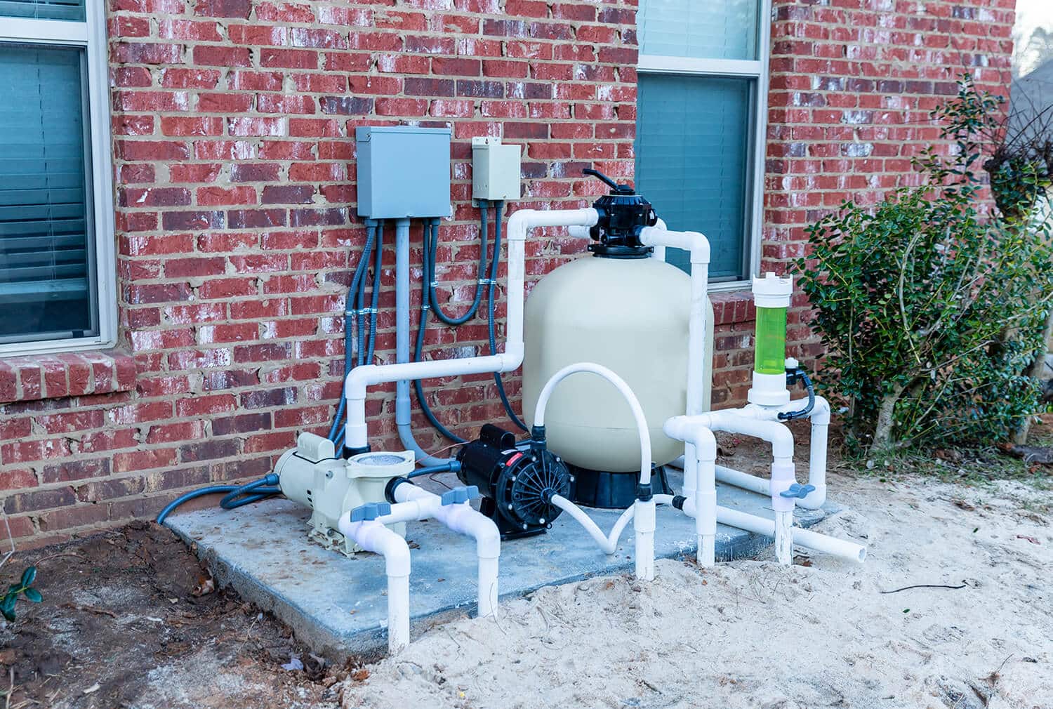 Complete pool filtration system showing the sand filter, pump, and PVC plumbing set up against a brick wall.