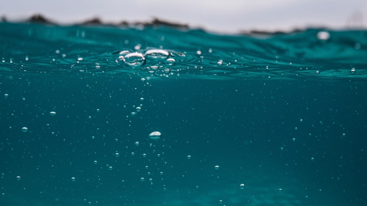 lose-up of a pool water surface showing a slight haze and bubbles caused by combined chlorine and contaminants.