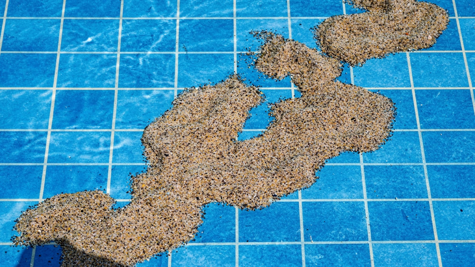 Fine sand and grit settling on the bottom tiles of a blue swimming pool.