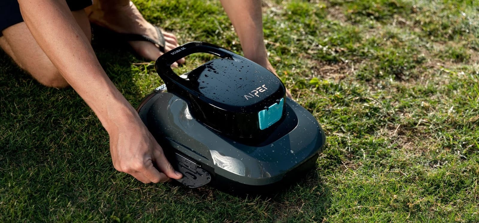 Aiper Scuba SE limpiador de fondo de piscina automatico inalámbrico siendo manipulado al aire libre sobre césped tras un ciclo de limpieza