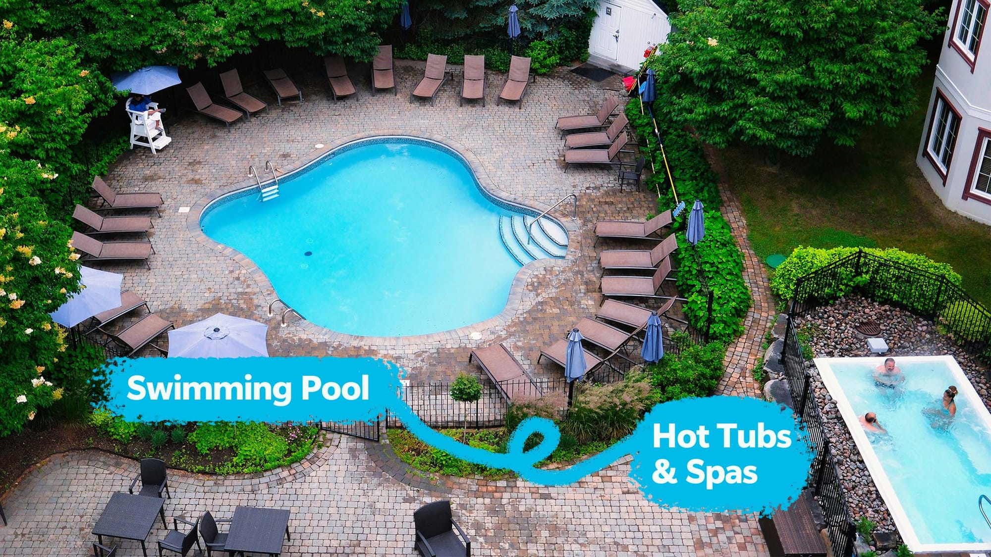 An aerial view of a hotel pool with hot tubs & spas, surrounded by lounge chairs and lush greenery.