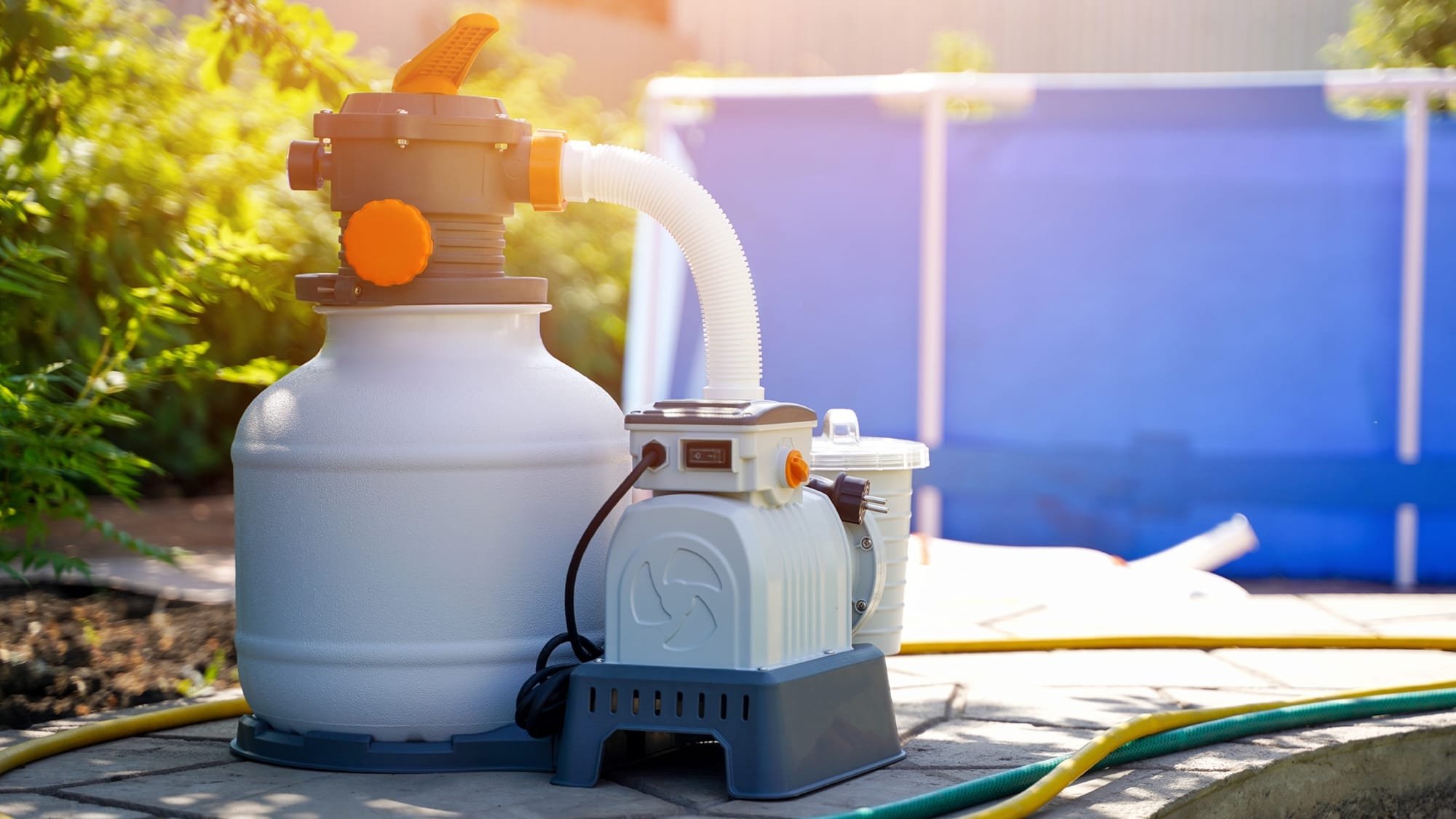 A sand pool filter and pump system are set up on a patio next to an above-ground pool.