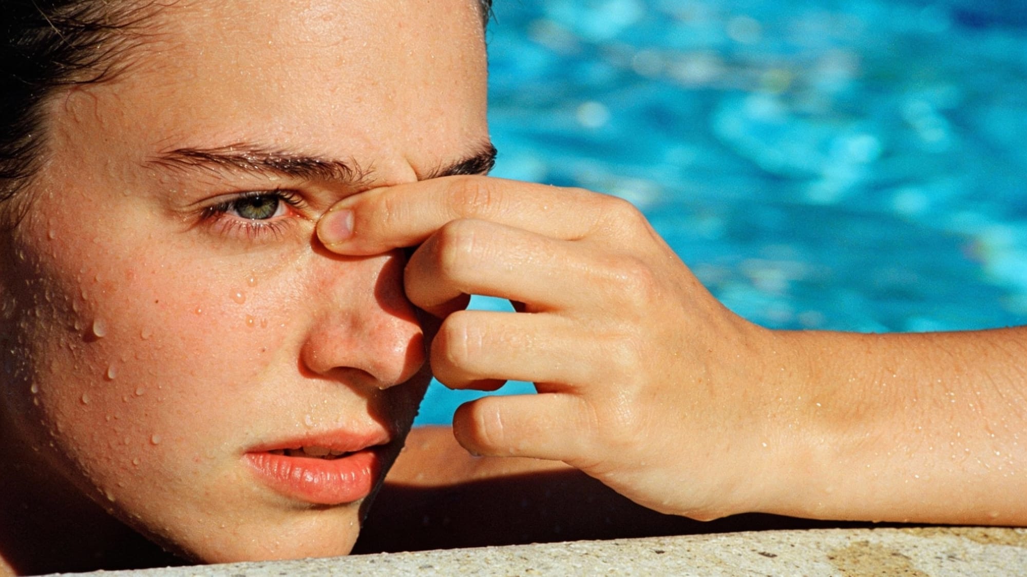 A swimmer rubbing her irritated eyes at the edge of a pool due to chemical imbalance.
