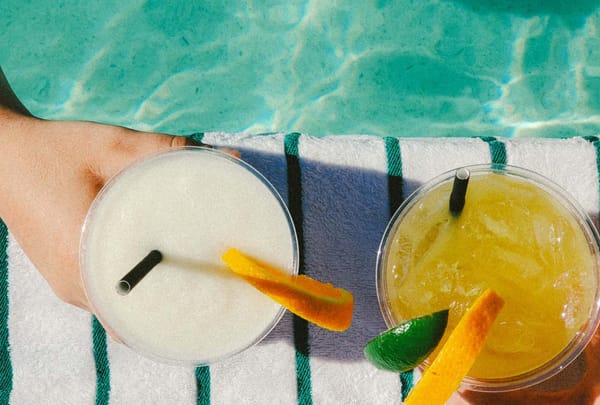 Two refreshing summer drinks with straws and citrus garnishes by a bright blue pool.