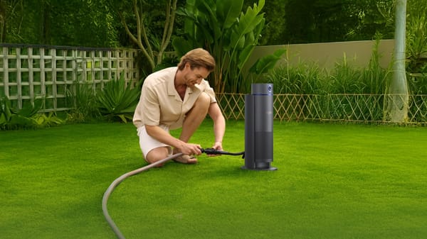 Homeowner connecting a hose to a smart irrigation controller device on a green lawn to automate watering.