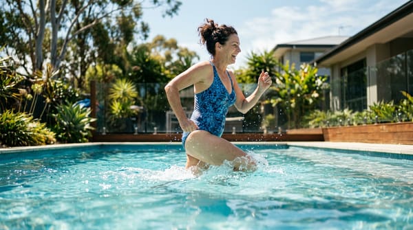 A woman smiling while doing swimming pool exercises by jogging in a sunny backyard pool.