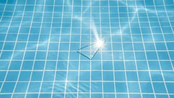 A sharp shard of broken glass on the bottom of a clear blue swimming pool, highlighting the hidden danger.