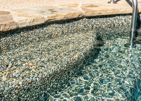 Close-up of textured Pebble Tec pool surface with clear water, showing the crevices that trap fine debris.