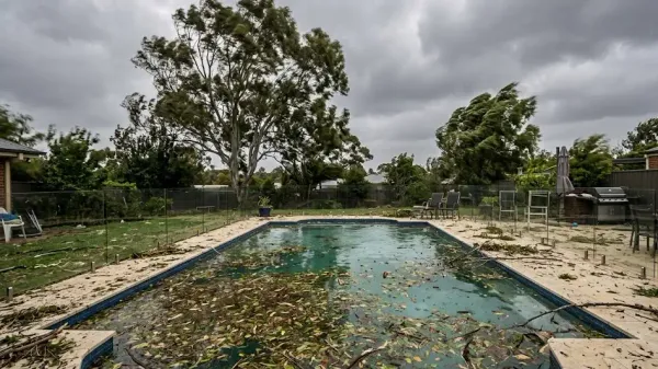 A backyard swimming pool covered in leaves and debris after a strong windstorm.